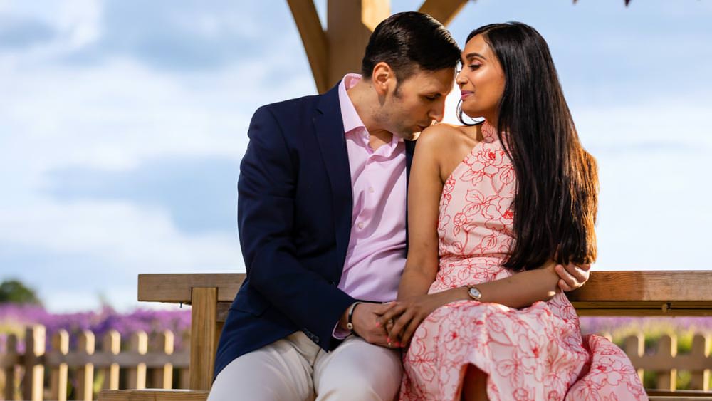 Indian couple on their engagement shoot. Groom kisses brides on her bare shoulders.